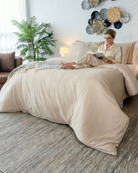 Dama sentada en una cama tendida con el Duvet Cover Dolcce Caramelo mientras lee un libro.